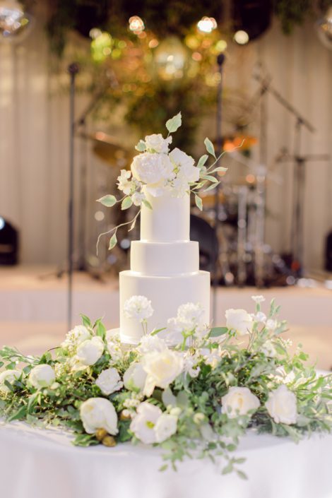 White wedding cake with sugar flower topper on a bed of fresh flowers