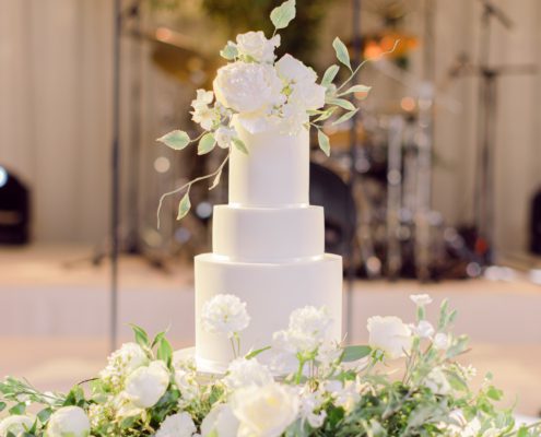 White wedding cake with sugar flower topper on a bed of fresh flowers