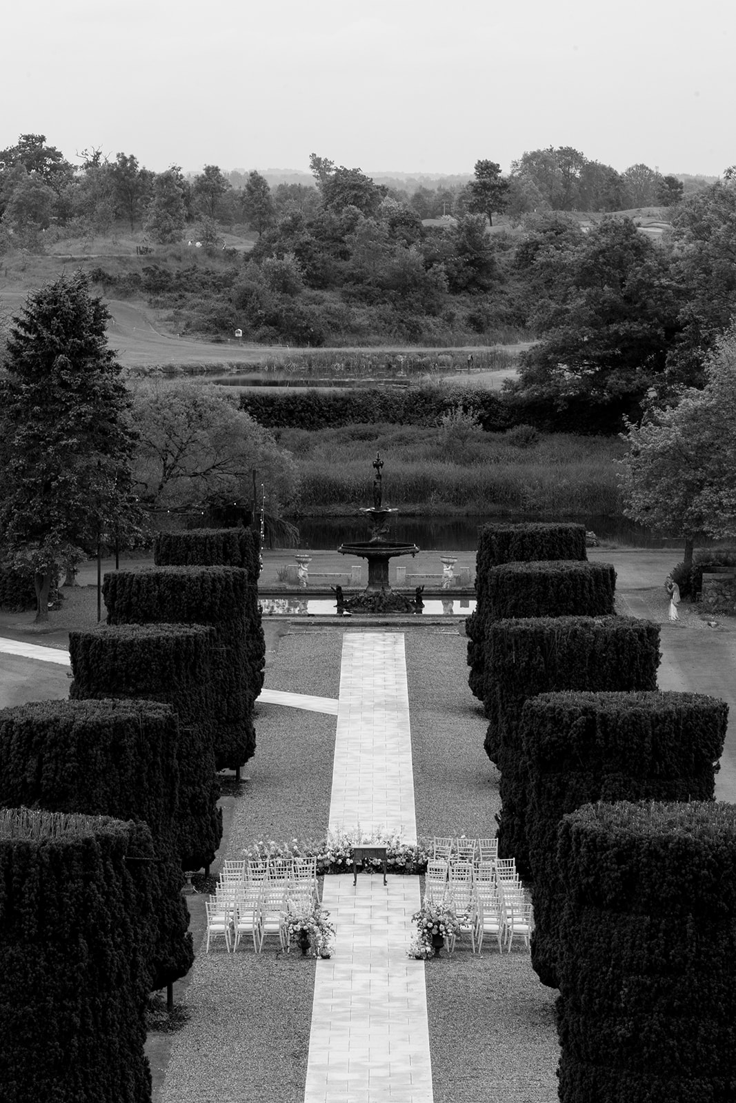 Drone footage of paved walkway between hedges with wedding ceremony set up along the route